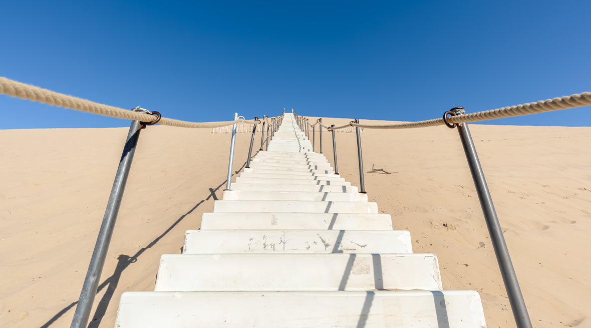 a staircase set into a high sand dune with metal pole and rope handrails